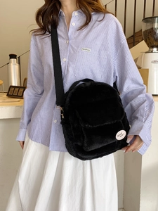 Mochila bandolera de felpa negra para mujer con parche 'Good Luck' en una cafetería