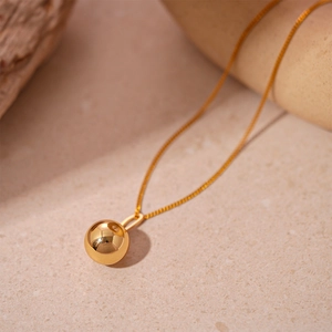 Gros plan détaillé d'un collier pendentif boule dorée poli miroir minimaliste
