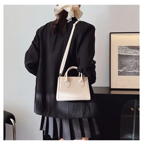 Detail of a creamy white rectangular PU leather handbag with detachable long strap and handles