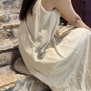 Silver heart-shaped mini bag with pearl chain shown on a model sitting on stone steps