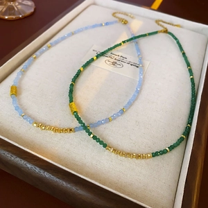 Détail de colliers en perles avec pierres bleu clair et vertes et accents dorés sur présentoir