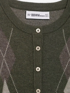 Dettaglio del cardigan in maglia verde con motivo a rombi, bottoni bianchi e scollo rotondo