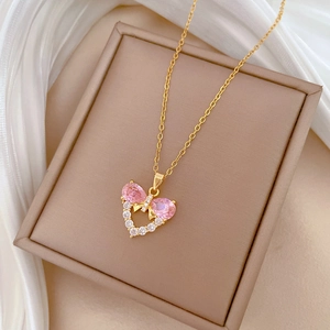 Close-up of golden bow-heart necklace with pink zircon stones on beige jewelry box