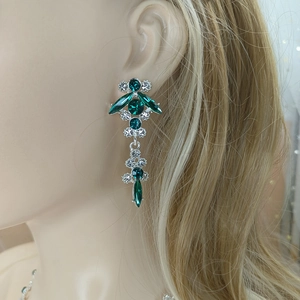 Close-up of elegant long crystal drop earrings with green and clear stones on a model