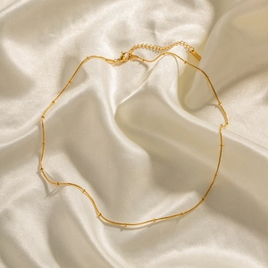 Detail of gold bead snake chain necklace with lobster clasp on white silk fabric