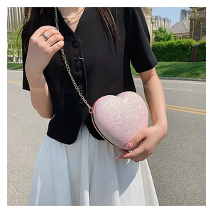 Detail of pink glitter heart bag with gold chain strap worn by a model in daylight