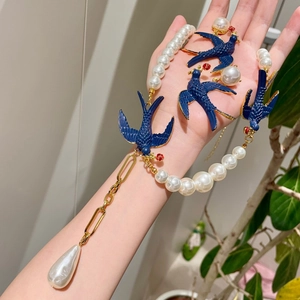 Close-up of vintage pearl necklace and bird earrings worn on model's arm