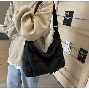 Close-up of a large black canvas crossbody tote bag worn by a model in a cozy library setting