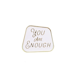Macro shot of white enamel brooch with golden You Are Enough lettering detail