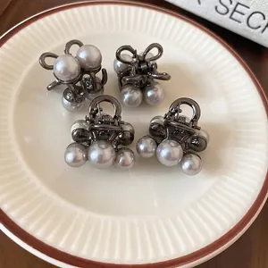 Mini pearl bow hair claw clips set in gunmetal finish on a white ceramic tray