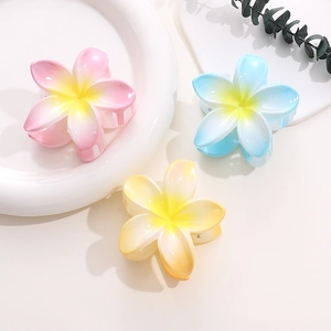 Flat lay of colorful gradient plumeria flower hair claws on a white decorative plate