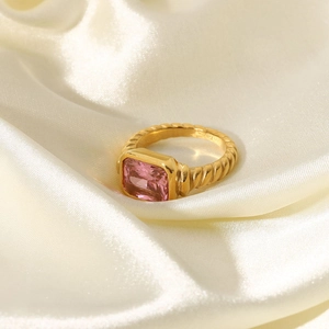 Detailed shot of a gold croissant ring with rectangular pink zircon on white silk