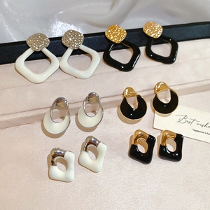 Makroaufnahme geometrischer Emaille-Ohrringe in Creme und Schwarz auf beigem Samt-Display