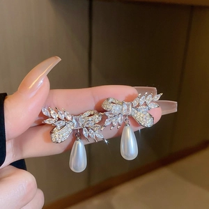 Close-up of sparkling bow earrings with zircon stones and teardrop pearl drops