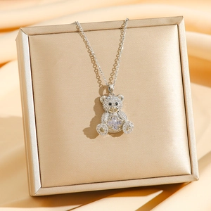 Silberne Teddybär-Halskette mit Kristallen und Kleeblatt-Detail auf einer Gold-Geschenkbox