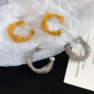 Detail of gold and silver twisted C-shaped hoop earrings on aesthetic white background