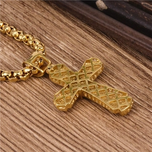 Macro shot of gold cross pendant with hollow diamond pattern and box chain on wood