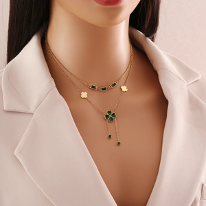 Double-layer gold necklace with emerald heart pendant and clover charm on a model