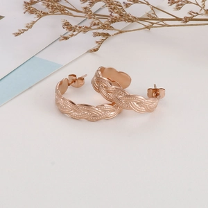 Detailed close-up of rose gold twisted texture hoop earrings on aesthetic background