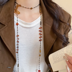 Close-up of amber and orange beaded necklace with a bow pendant on a model