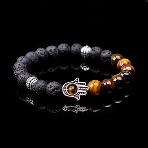 Macro shot of lava rock beads and tiger eye stones with Hamsa Hand charm on black reflection