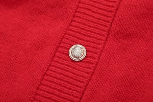 Detail einer roten Strickjacke mit einem verzierten, silbernen Relief-Metallknopf