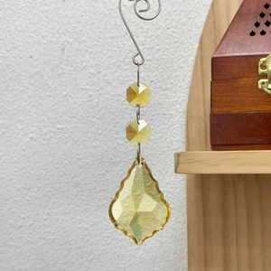 Close-up of yellow crystal teardrop pendant with hexagonal beads on a metal hook