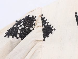 Detail of black geometric embroidery on beige linen dress sleeve and shoulder area