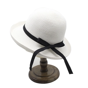 White straw sun hat with black ribbon bow on a wooden stand for summer vacation wear