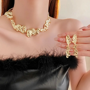 Close-up of irregular crumpled gold metal necklace and earrings set on black feathers