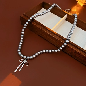 Vue détaillée du collier de perles grises avec pendentif nœud argenté et chaîne réglable