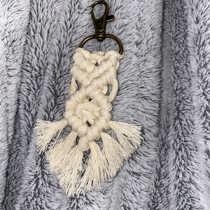 Handmade beige macrame keychain with bronze lobster clasp on textured grey background