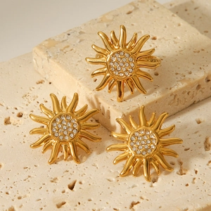Golden sun-shaped earrings set with sparkling crystals on a natural stone background