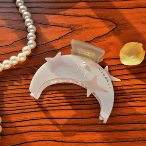 Macro detail of crescent moon hair claw clip with star patterns, pearls, and rhinestones