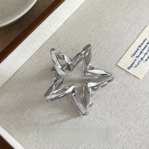 Silver star-shaped metal hair claw clip with 6cm length shown on textured fabric