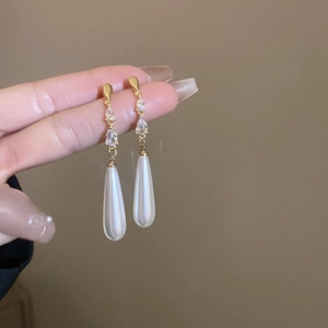 Détail de boucles d'oreilles à pompons dorés avec cristal goutte et longue perle