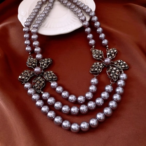 Detail of triple-layer pearl necklace featuring crystal-encrusted hollow flower charms