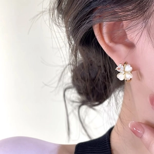 Close-up of golden clover earrings with pearly petals and small crystal center on ear