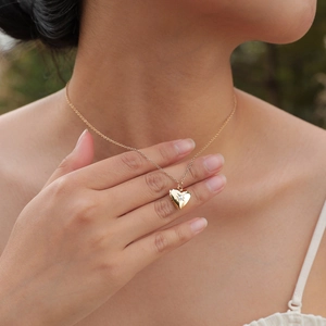 Close-up of gold heart locket necklace with crystal on model's neck for elegant styling