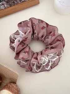 Vue détaillée d'un chouchou rose à fleurs avec dentelle blanche sur fond minimaliste