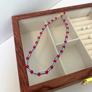 Detail of beaded necklace with red and blue striped beads in a wooden jewelry box