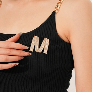 Detailed close-up of a luxury M-shaped brooch with white rhinestones on a black top