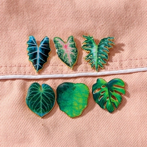 Tropical green enamel leaf brooches with gold plating on pink denim fabric background