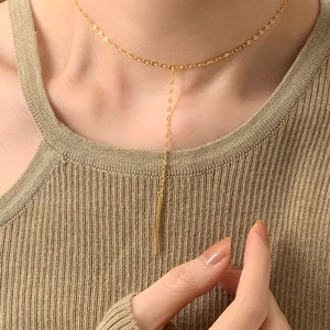 Detail of a minimalist gold Y-shaped necklace with a long bar pendant on a female model