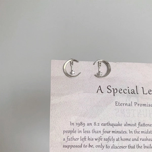 Minimalist silver moon stud earrings with zircon crystals on a jewelry display card