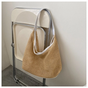 Detail of khaki woven hobo bag with white wide straps hanging on a minimalist chair