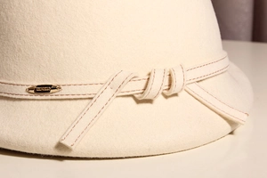 Detail of cream wool felt bucket hat featuring decorative stitching and gold metal buckle