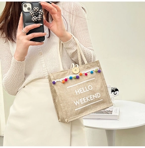 Detail of jute tote bag with HELLO WEEKEND text, colorful pom-poms and lace trim