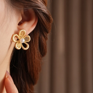 Gros plan de boucles d'oreilles fleur évidée dorée avec perle portées par un mannequin