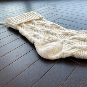 Classic cream cable knit Christmas stocking with hanging loop on dark wood background